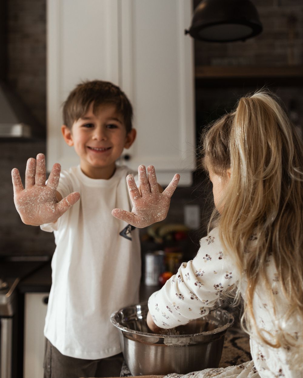 A child shows flour-covered hands while baking in a modern kitchen.