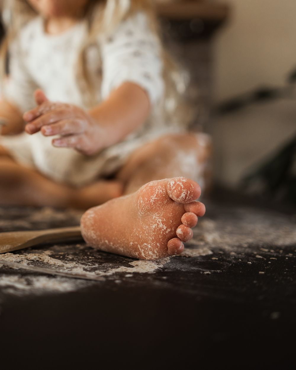 Close-up of small flour-covered foot on dark counter while baking.