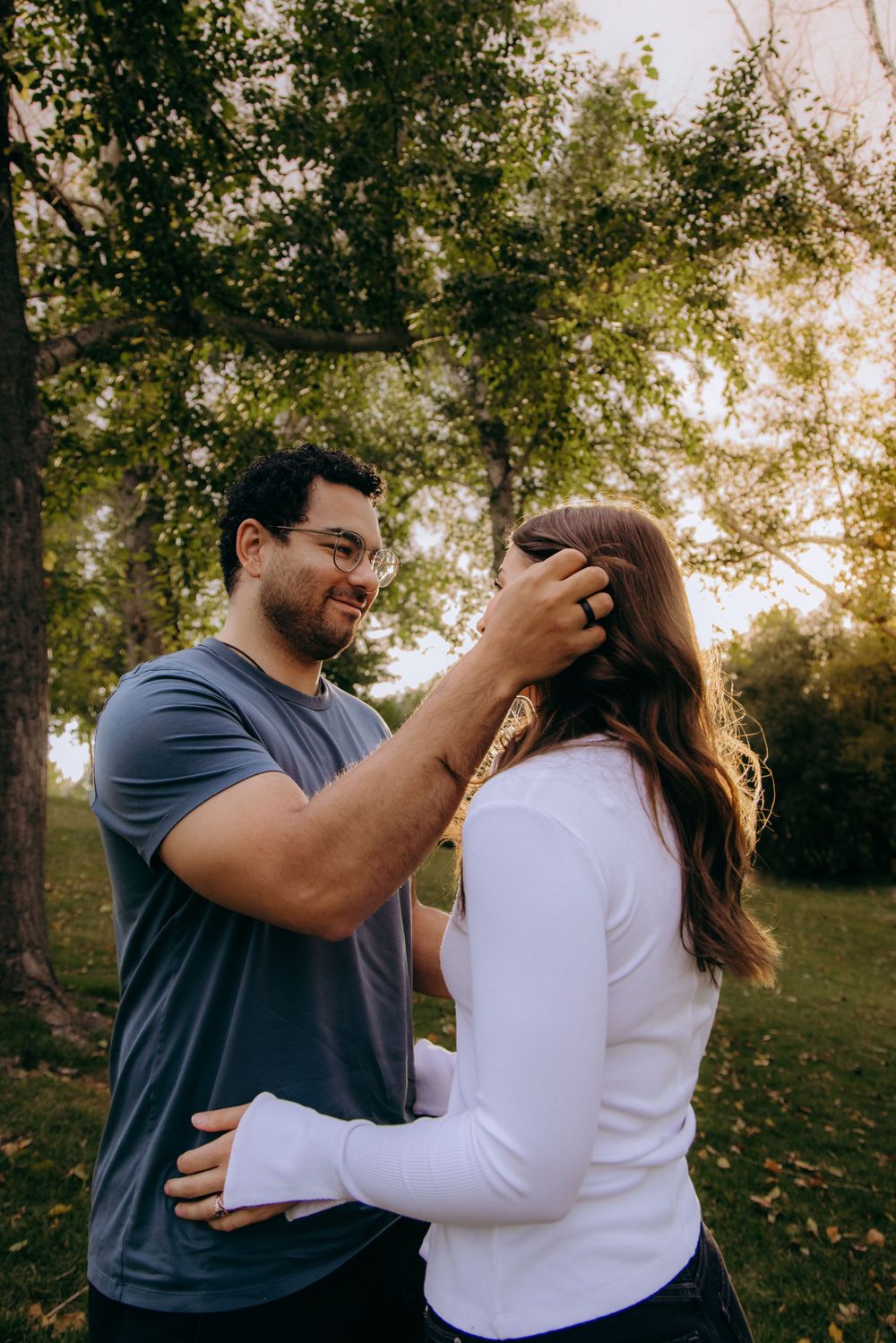 Couple shares tender moment in park during golden hour with trees in background.