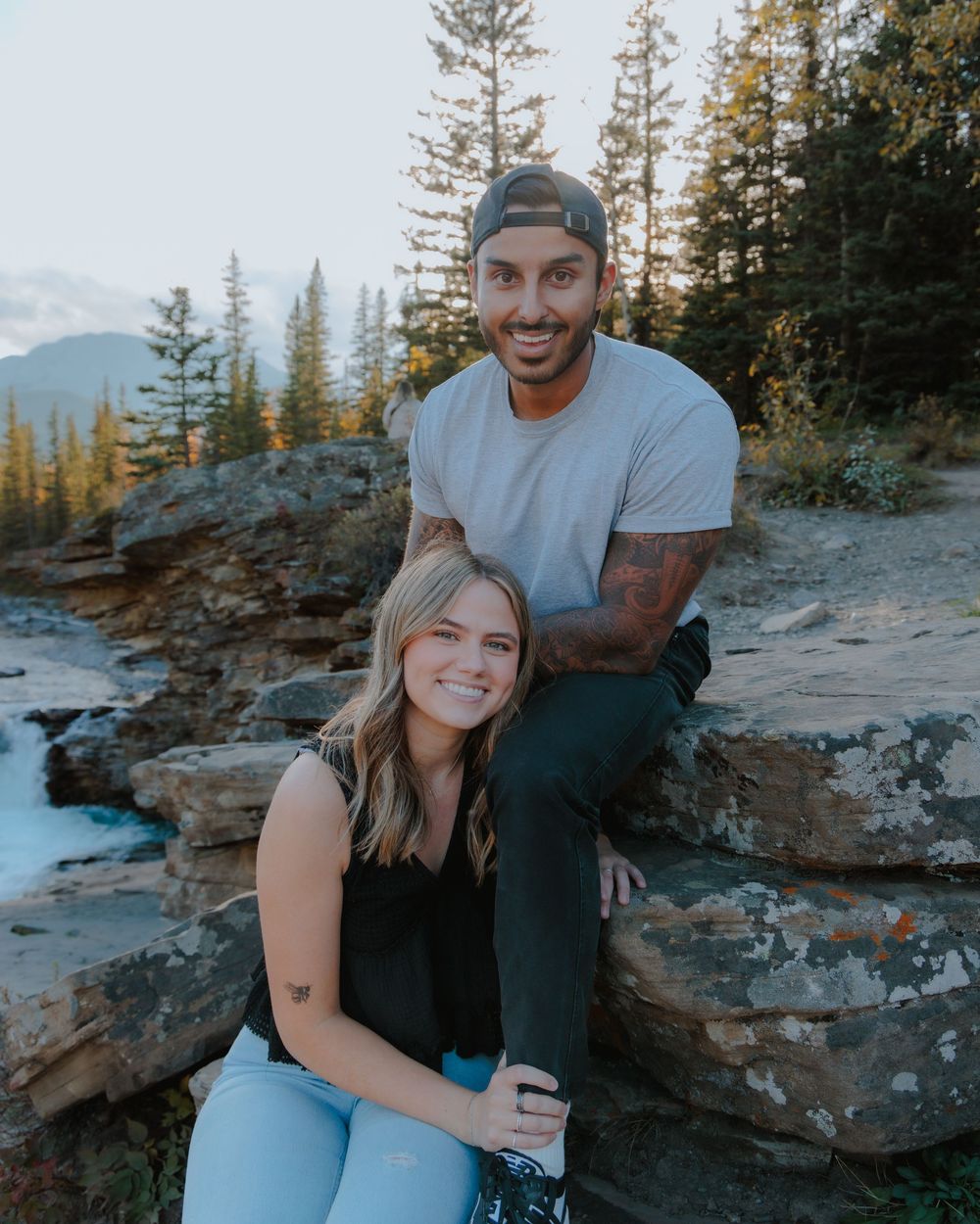Happy couple shares candid moments while sitting on rocky mountain terrain.
