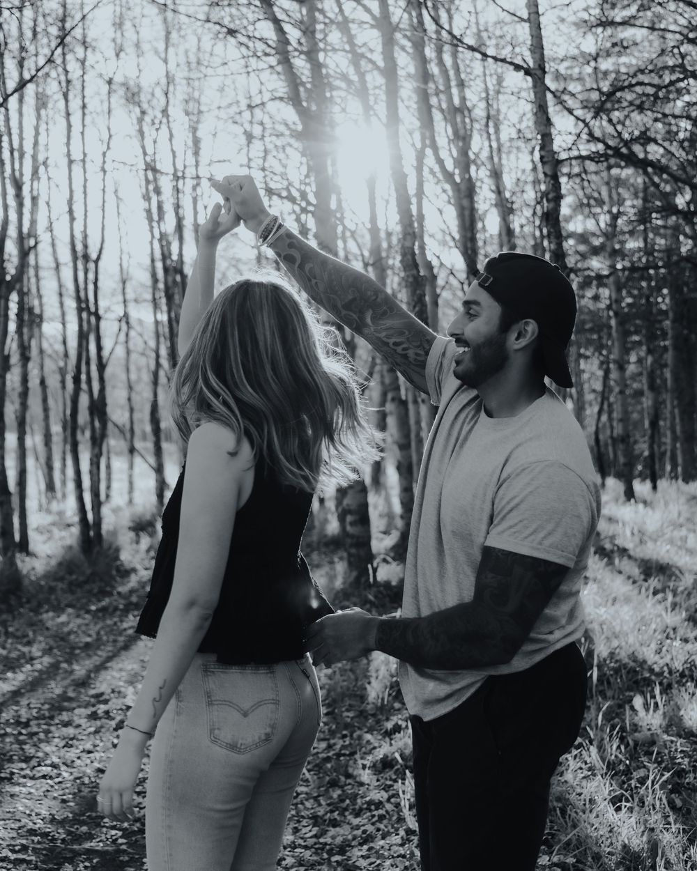 Black and white photo of a couple sharing intimate moments in a forest setting.