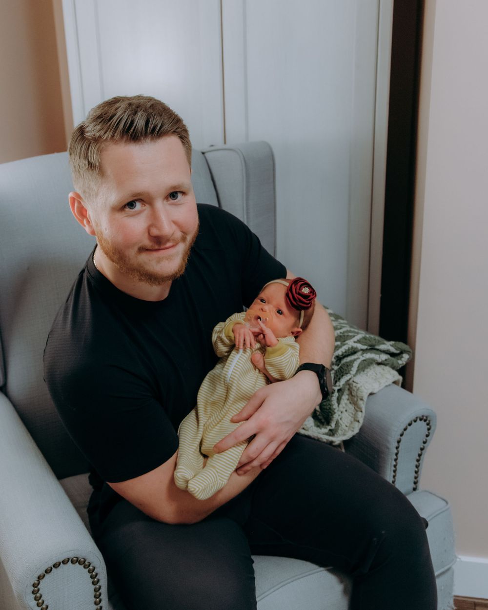 Parent in black shirt holding newborn baby in cozy nursery chair.