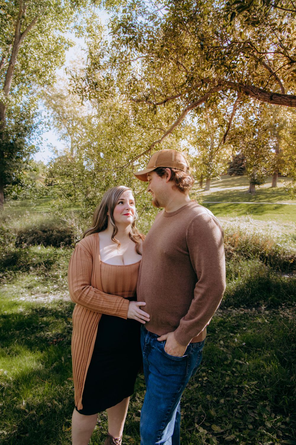 Couple sharing intimate moments together in a sun-dappled outdoor setting.