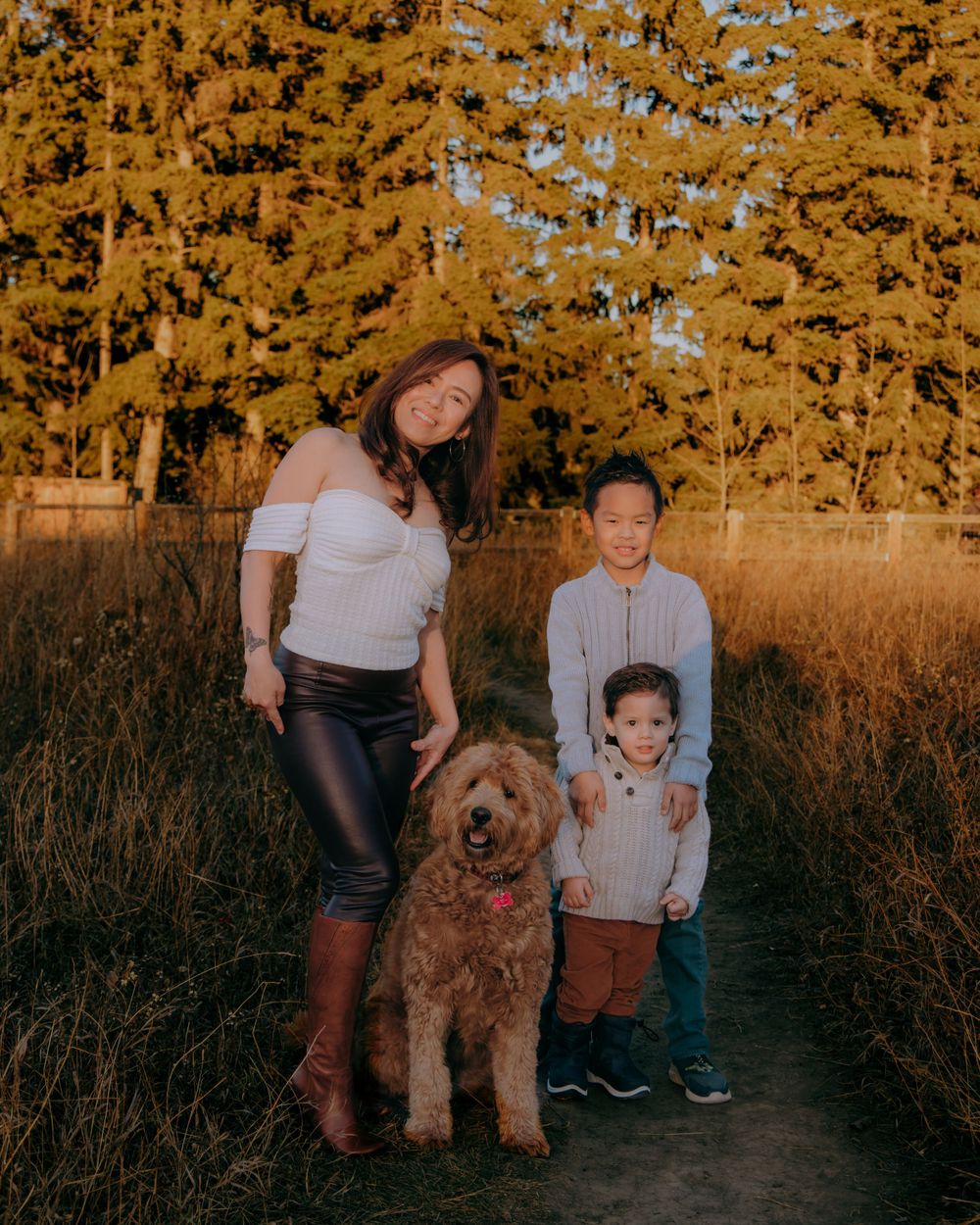 A large fluffy goldendoodle dog poses with people in an autumn field at sunset.