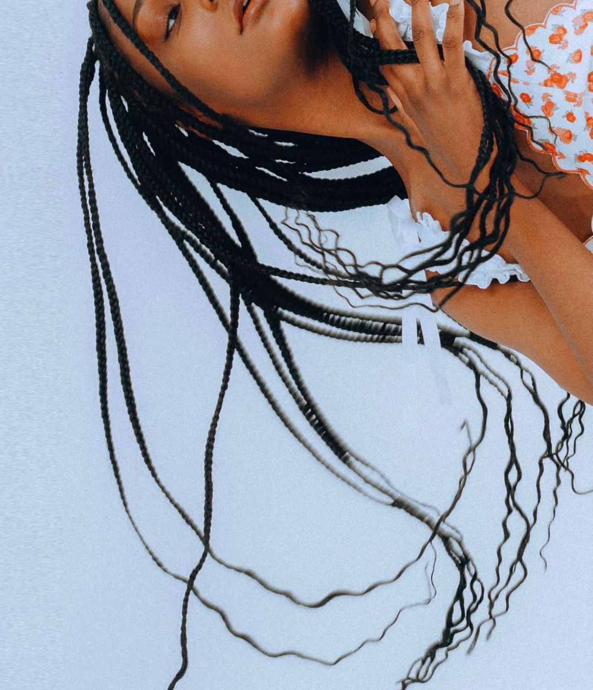 An artistic portrait featuring long dark braids against a light blue background with coral accents.
