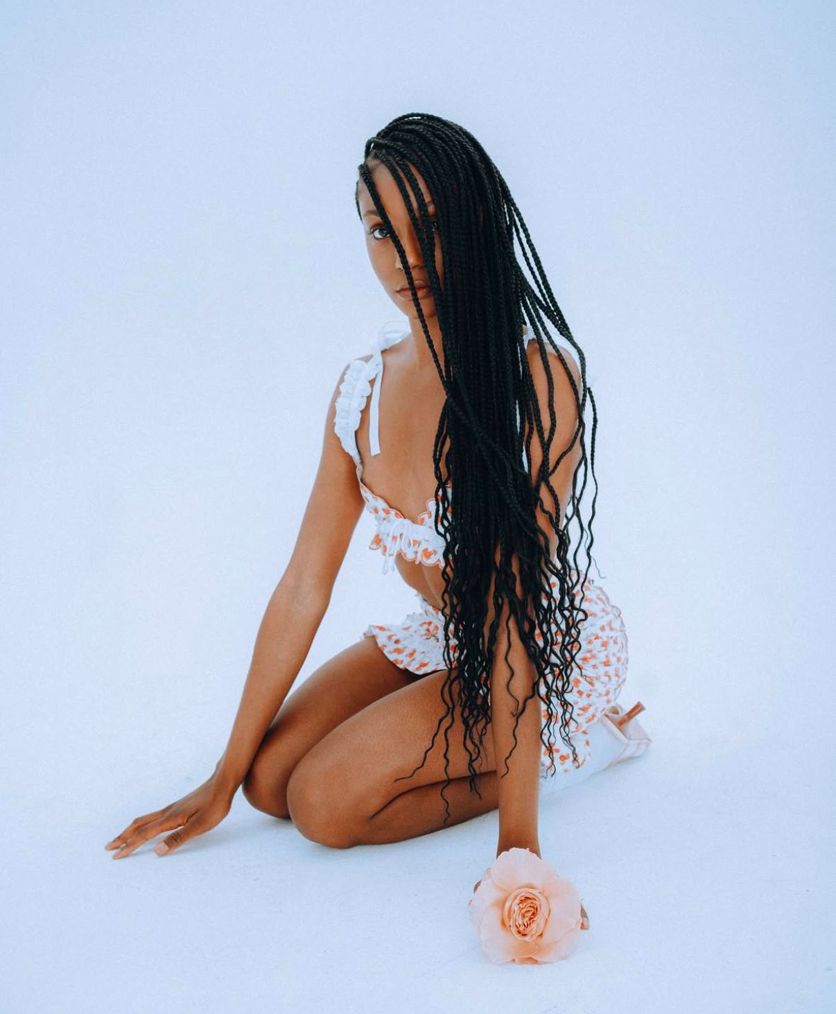 Graceful pose on white background wearing delicate lace lingerie with coral flower accents.