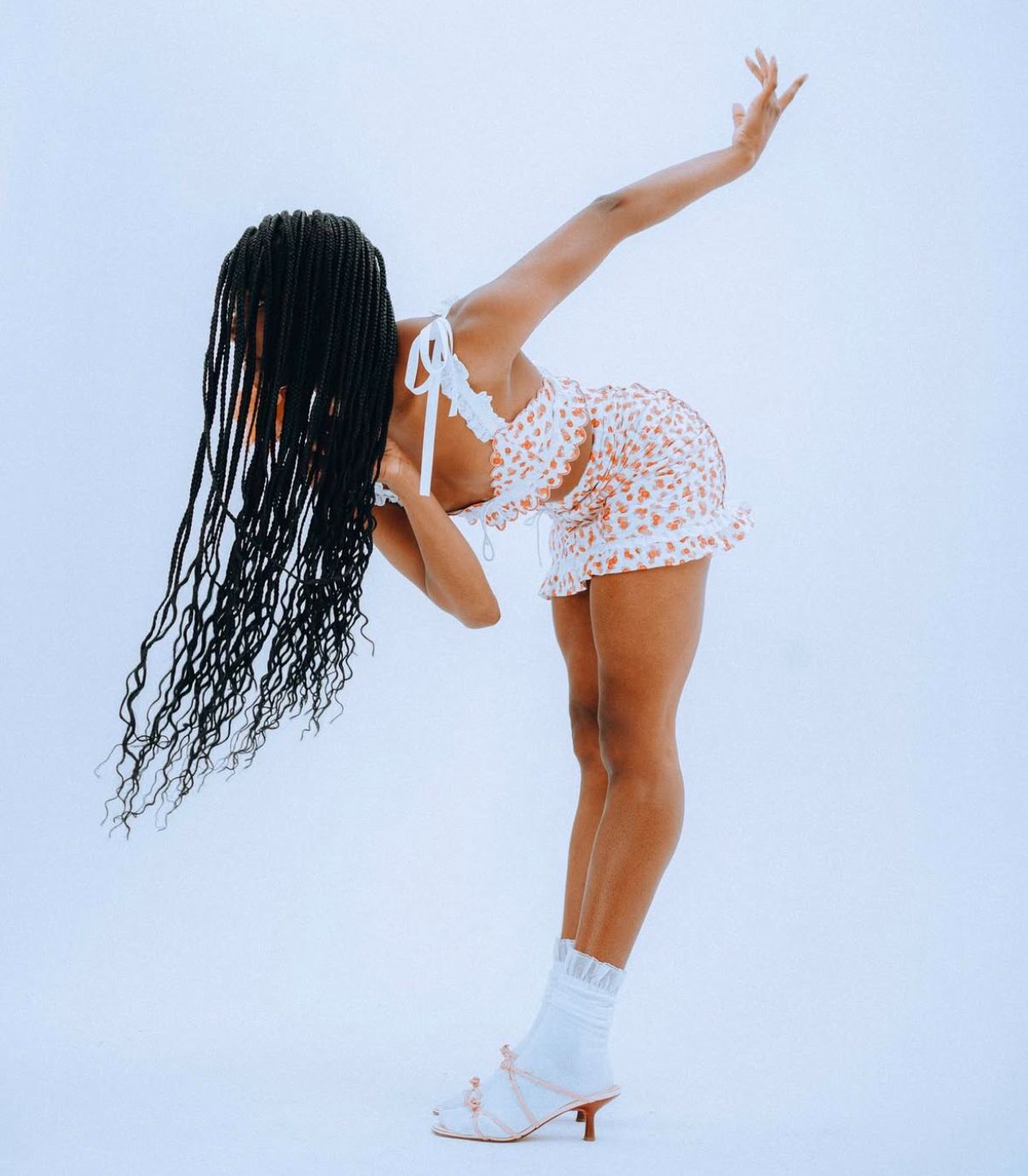 Dynamic dance pose featuring white heels and lace outfit against minimal background.