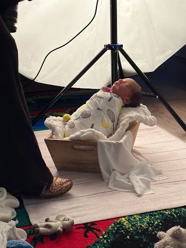 Newborn baby swaddled in patterned blanket resting in wooden crate during professional photo shoot.
