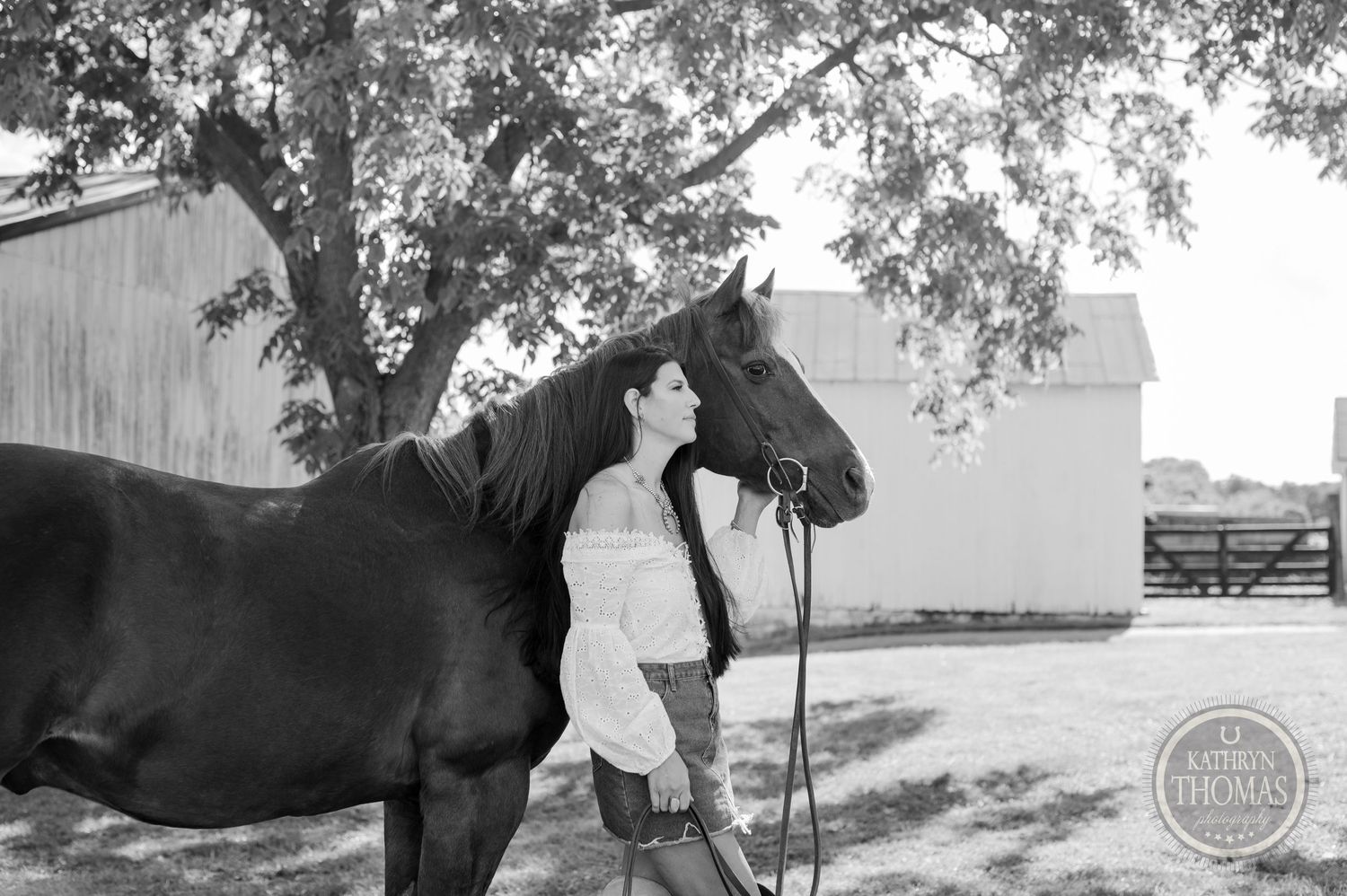 Black and white portrait of a horse and companion near a white barn under trees.