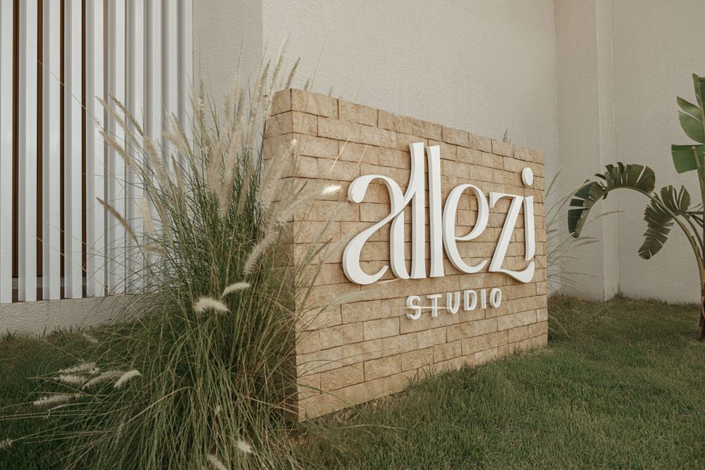 Sign reading 'alezi studio' mounted on textured stone wall with ornamental grasses.