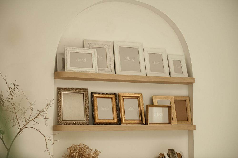 Collection of empty picture frames arranged on wooden shelves in arched alcove.