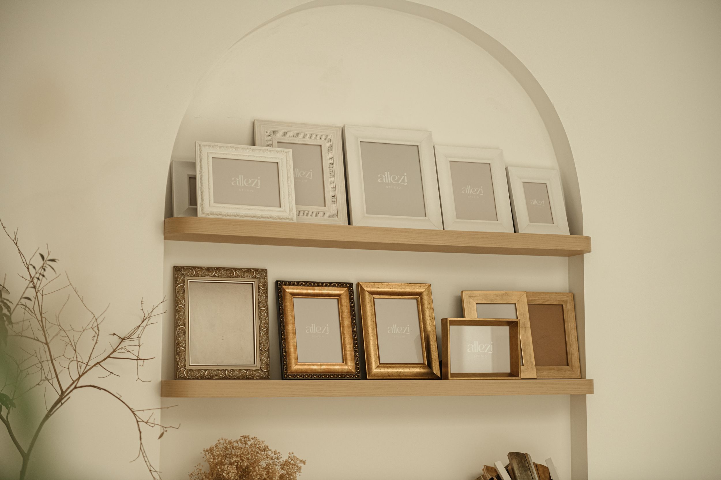 Collection of empty picture frames arranged on wooden shelves in arched alcove.