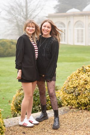 Friends pose together on a misty day outside a stately building with manicured gardens.