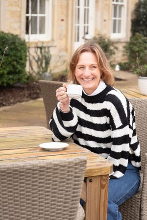 Someone wearing a black and white striped sweater enjoys coffee outdoors at a wooden table with wicker chairs.