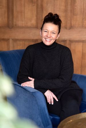 Person wearing black turtleneck sits comfortably on a blue upholstered couch against wooden paneled wall.