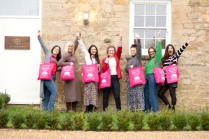 A group of people jumping and celebrating while holding pink retail shopping bags outside a stone building.