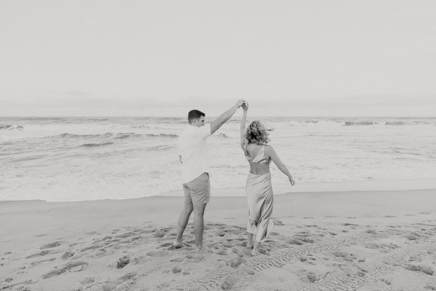 Black and white photo of couple dancing on beach.