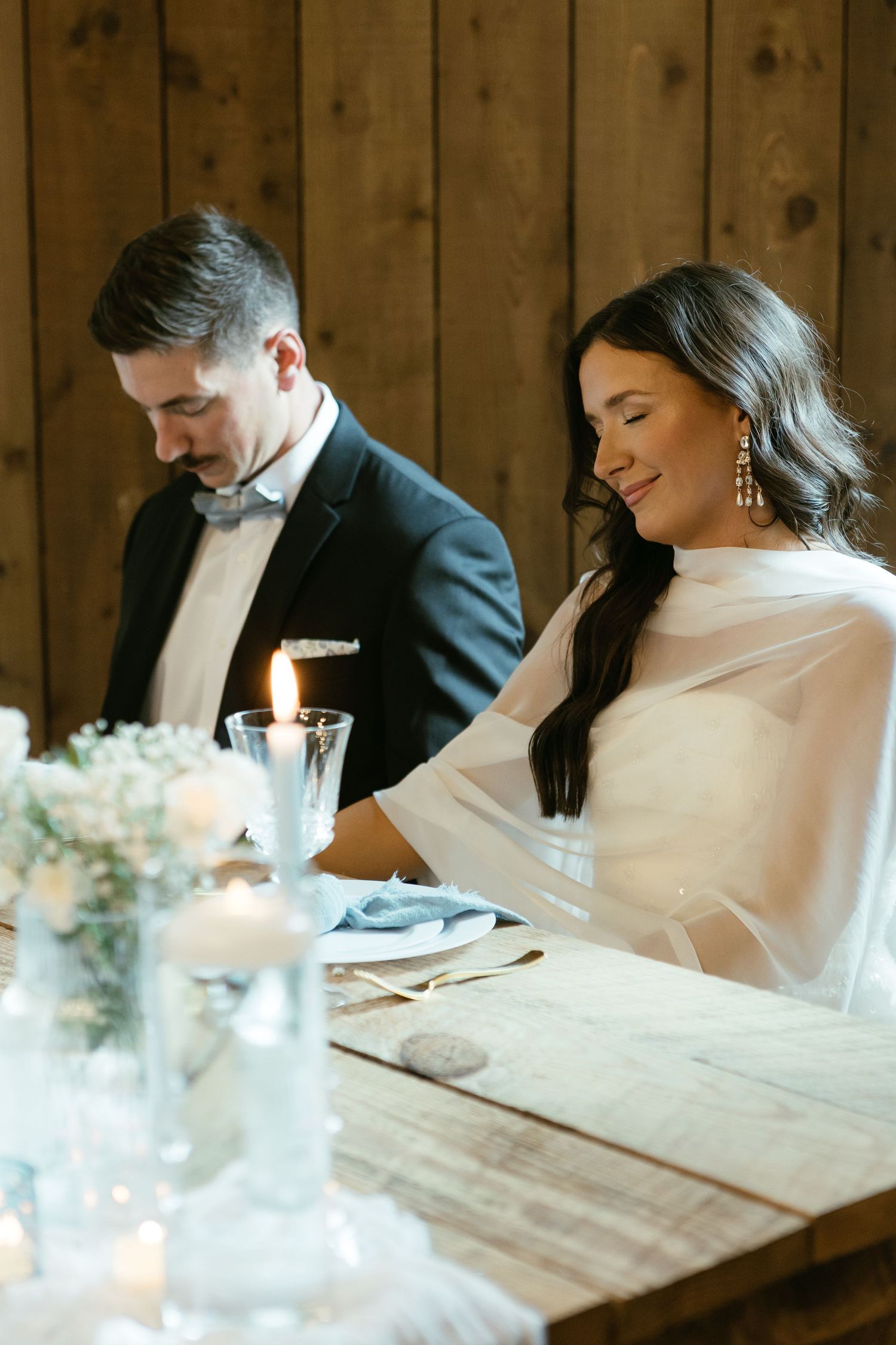A couple sits together at an elegant rustic wooden table during their wedding reception.