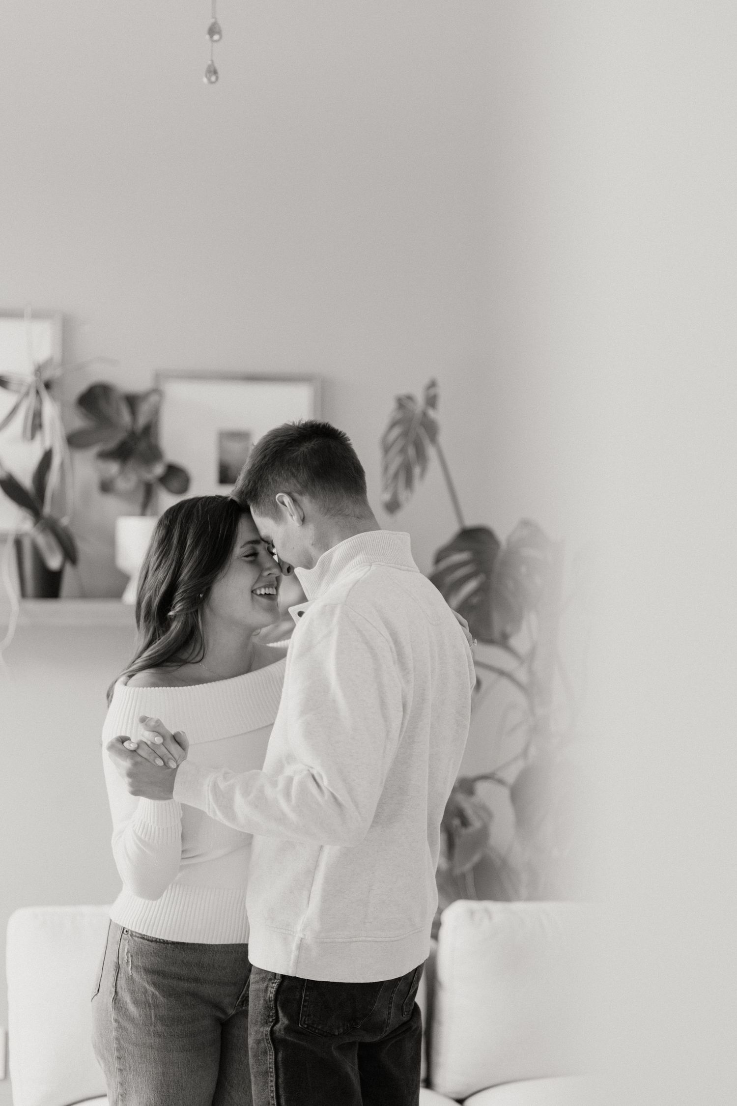 Intimate black and white photo of couple embracing in minimalist room with wall art.