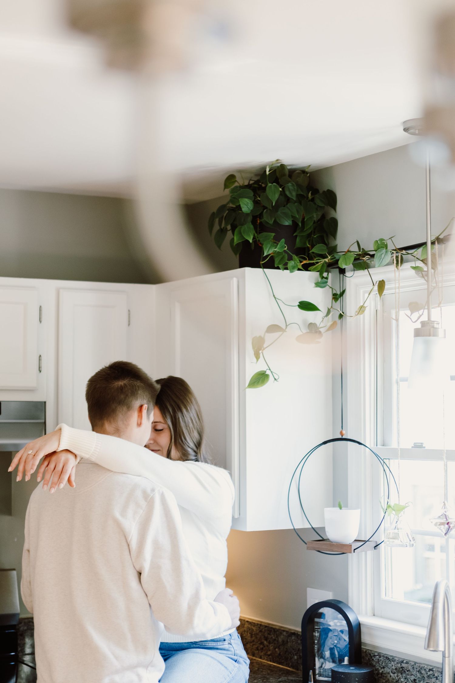 Romantic couple embracing in bright modern kitchen with hanging plants.