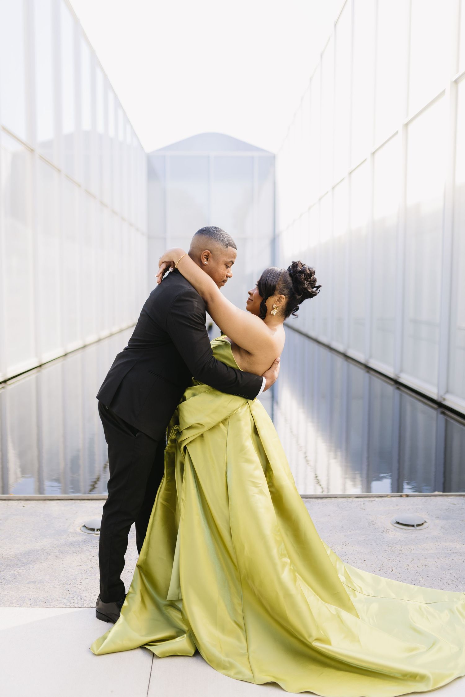A couple embraces in formal attire, with the woman wearing a striking lime green ball gown with a flowing train.