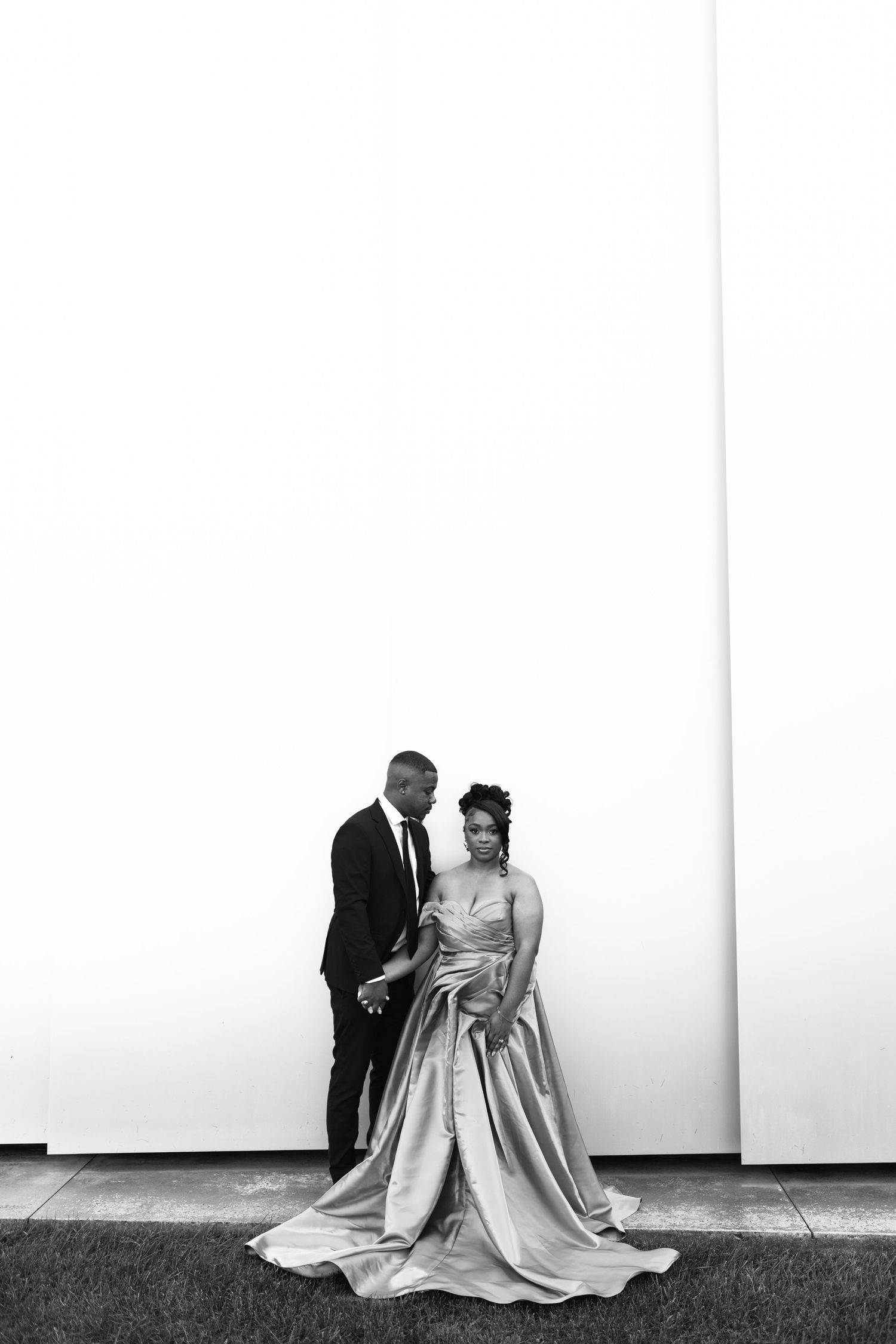 A minimalist black and white wedding portrait against a white wall.