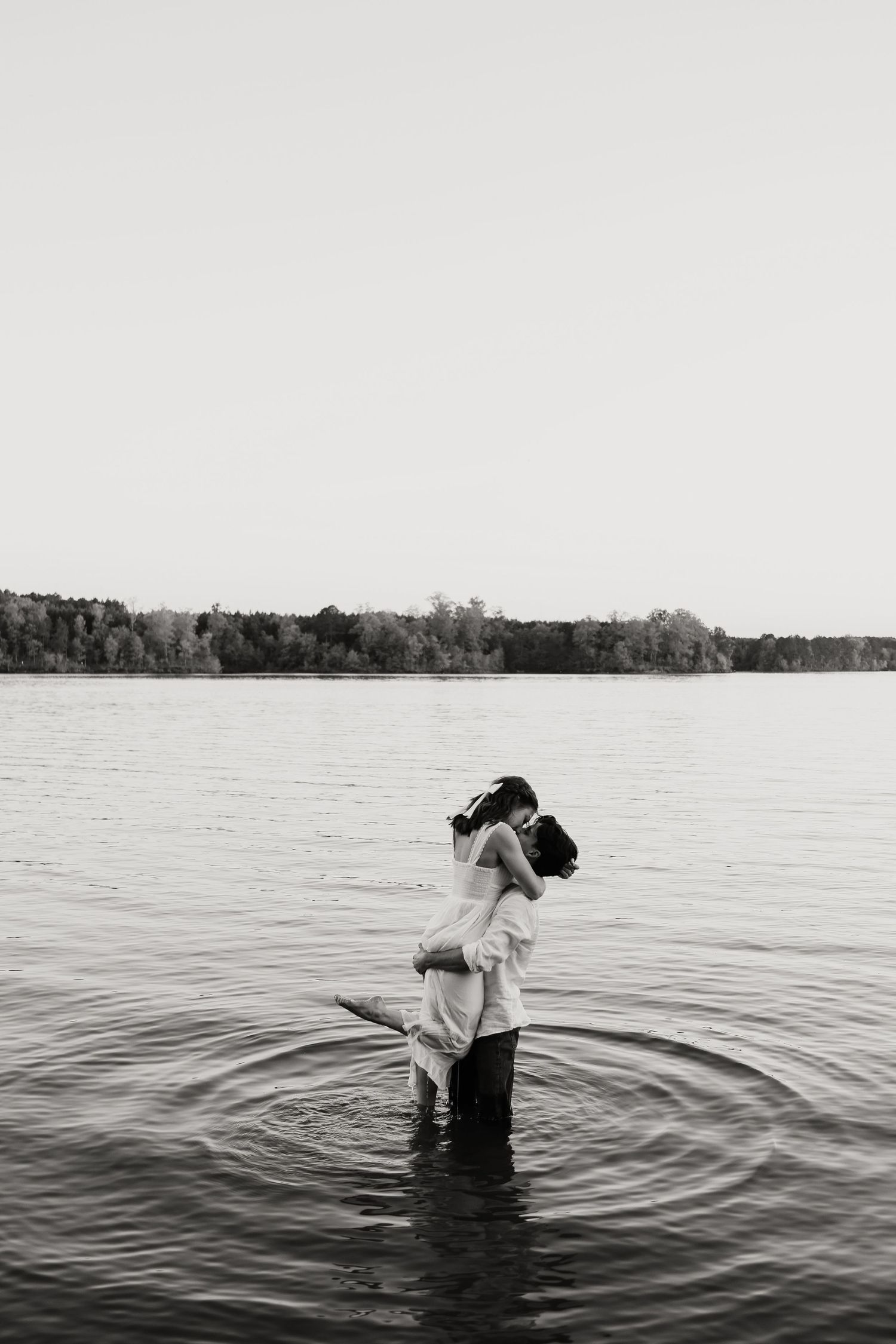 A black and white sequence of someone wading and dipping into a serene lake or body of water.