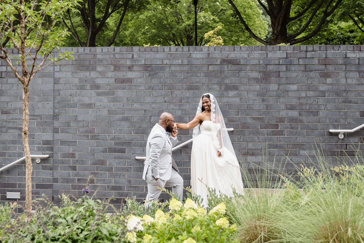 A couple shares a tender moment in a modern garden setting with grey stone walls.