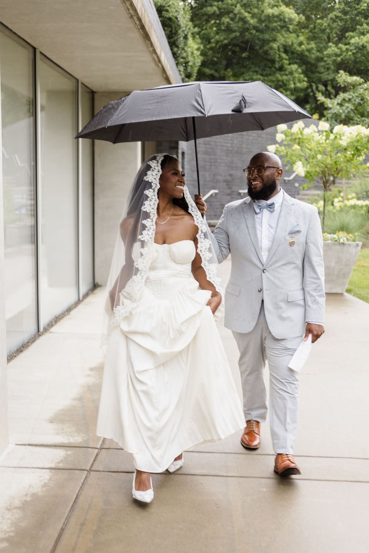 A couple walks under a black umbrella along a covered walkway.