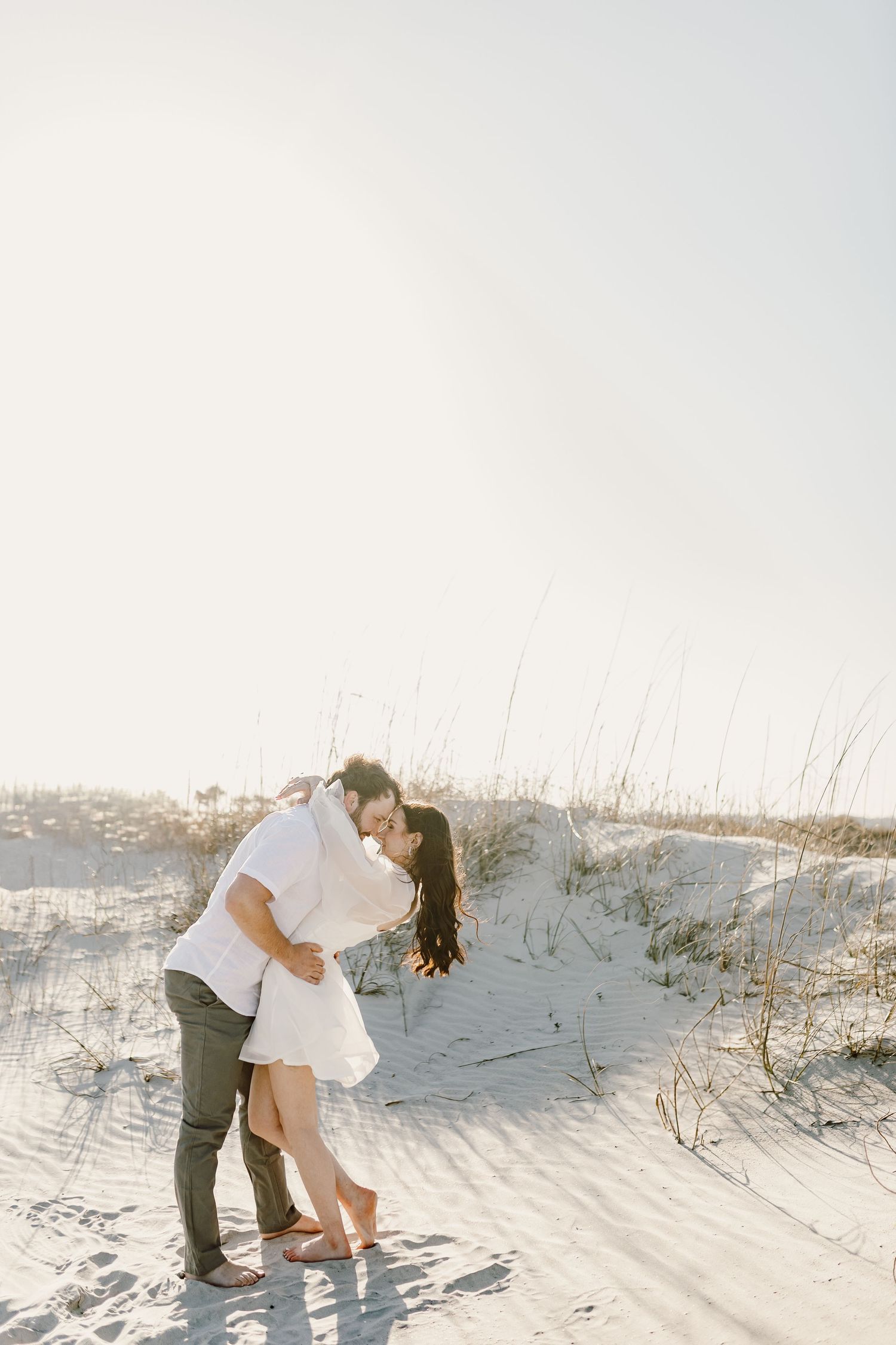 Romantic moment between couple on white sand dunes at sunset.