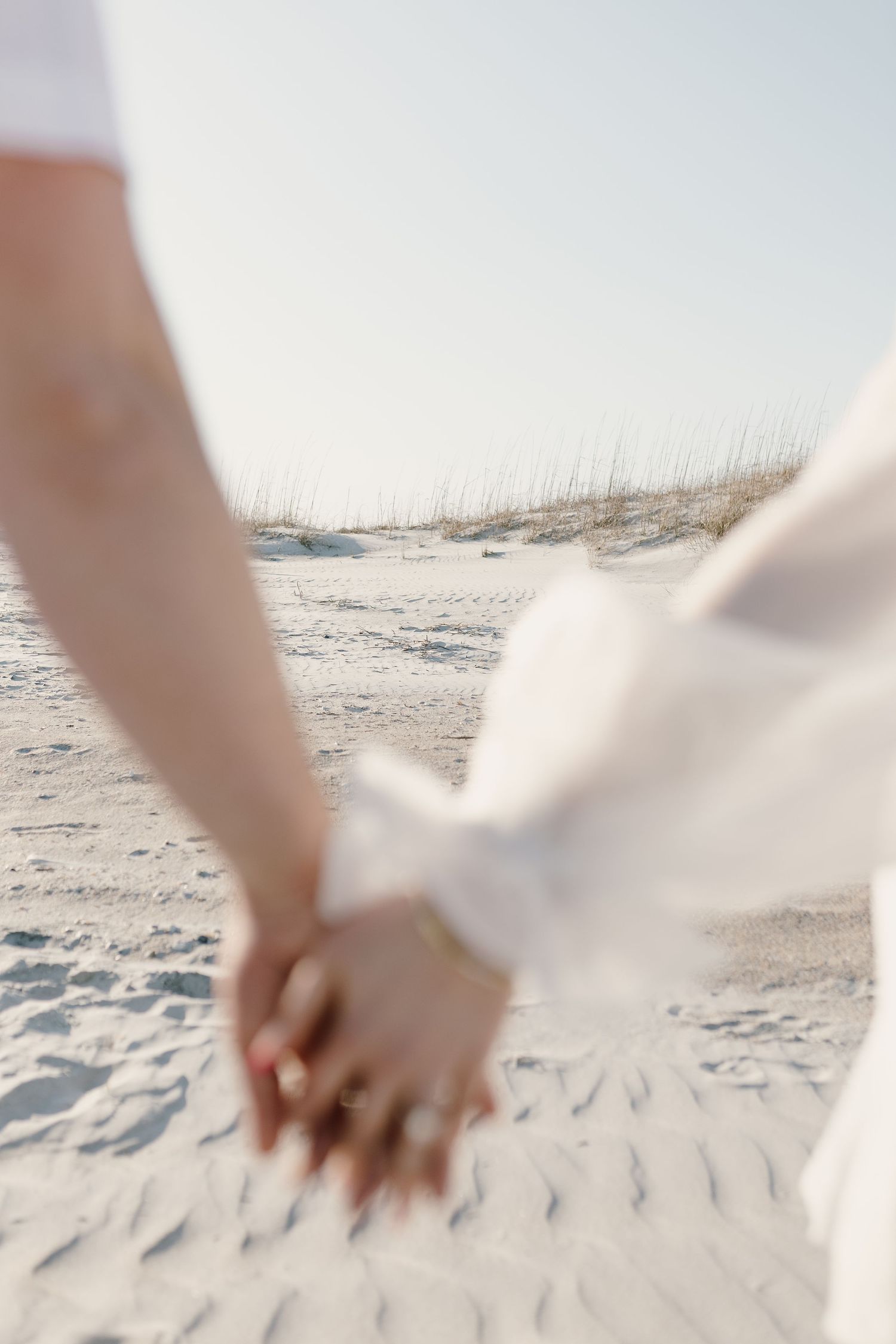 Close-up of intertwined hands against sandy beach background.