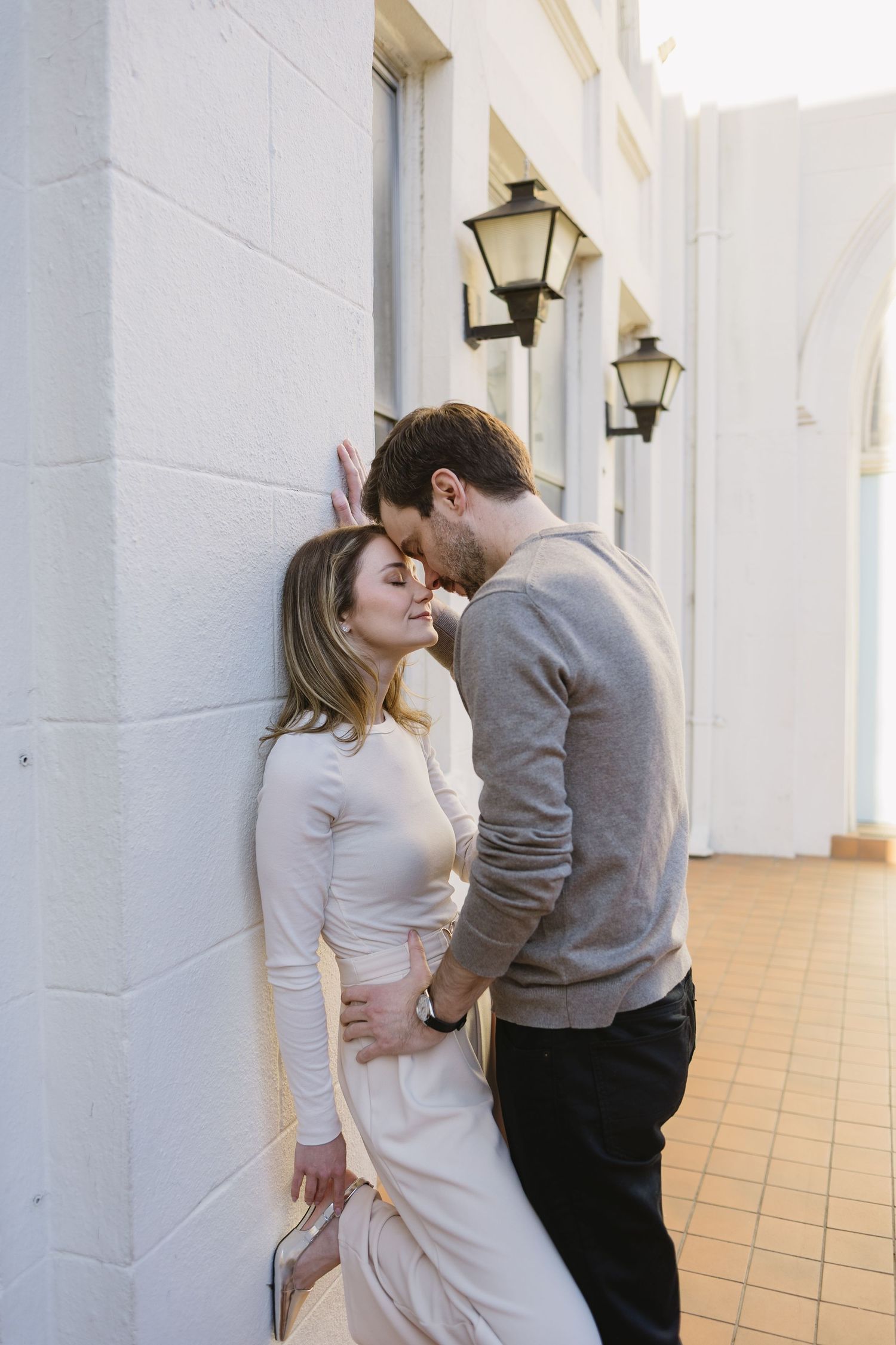 Romantic couple sharing intimate moment in white tiled hallway with lanterns.