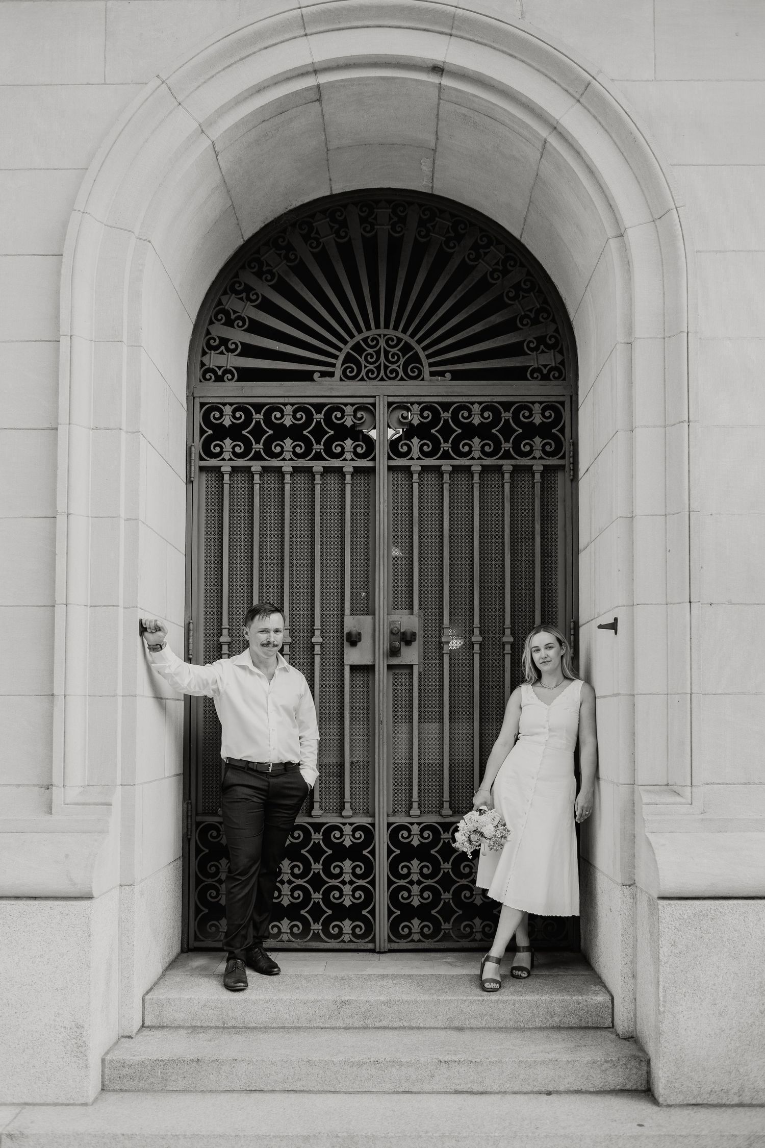 A couple poses in a classic archway with ornate iron gates.