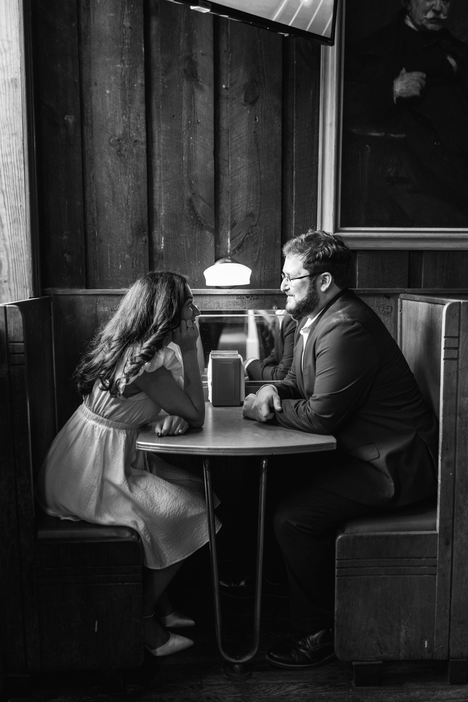 A moody black and white photo of people sitting in booths at a dimly lit restaurant or bar.