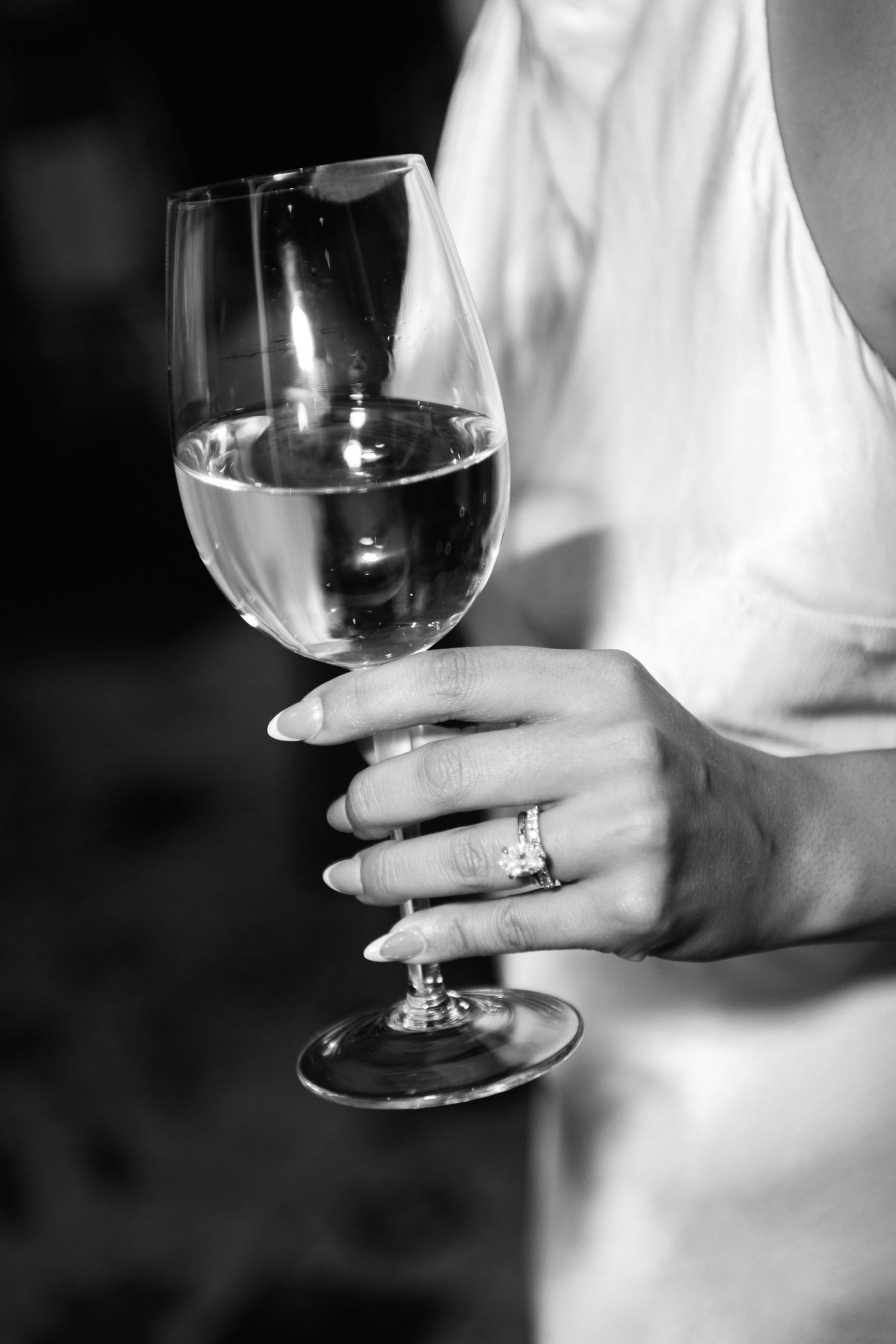 A hand holding a wine glass shows off an elegant engagement ring.