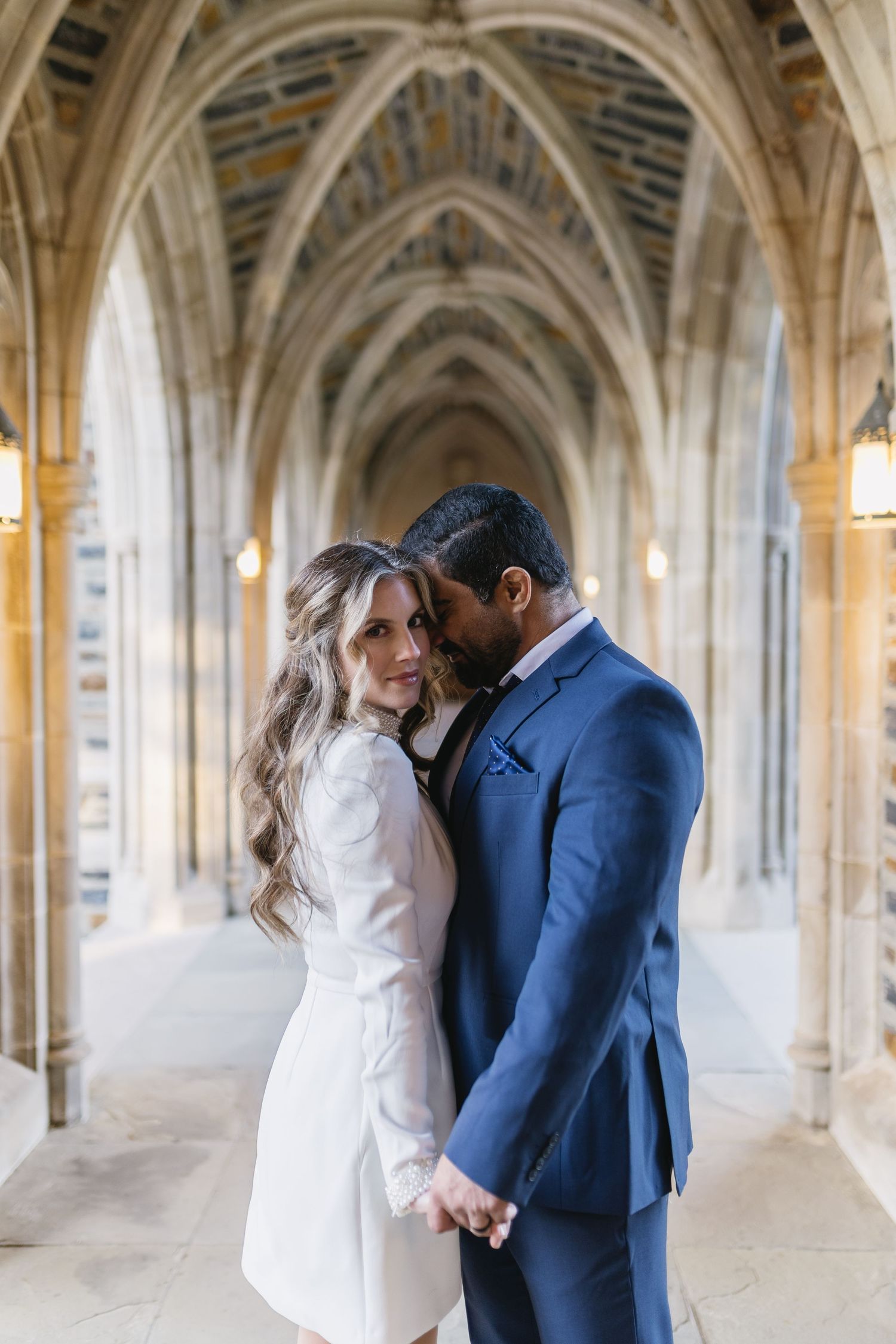 A couple shares an intimate moment under Gothic stone archways with warm lighting.