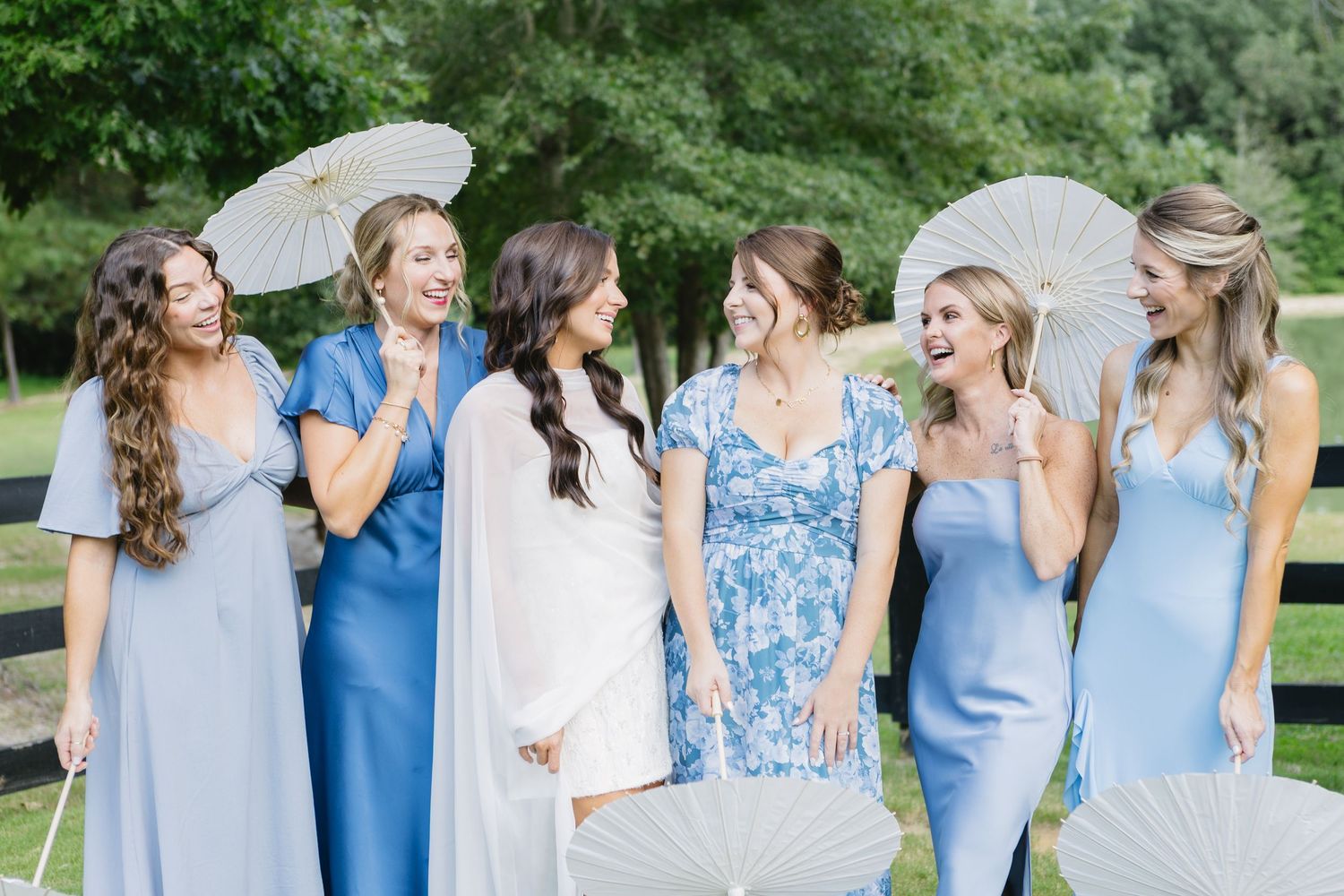 Bridesmaids in light blue dresses pose together outdoors on a sunny day.