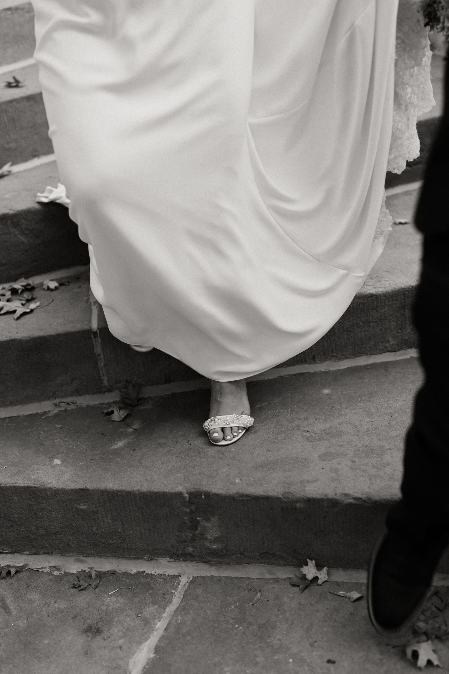 Black and white photo of dress hem and shoes on stone steps.