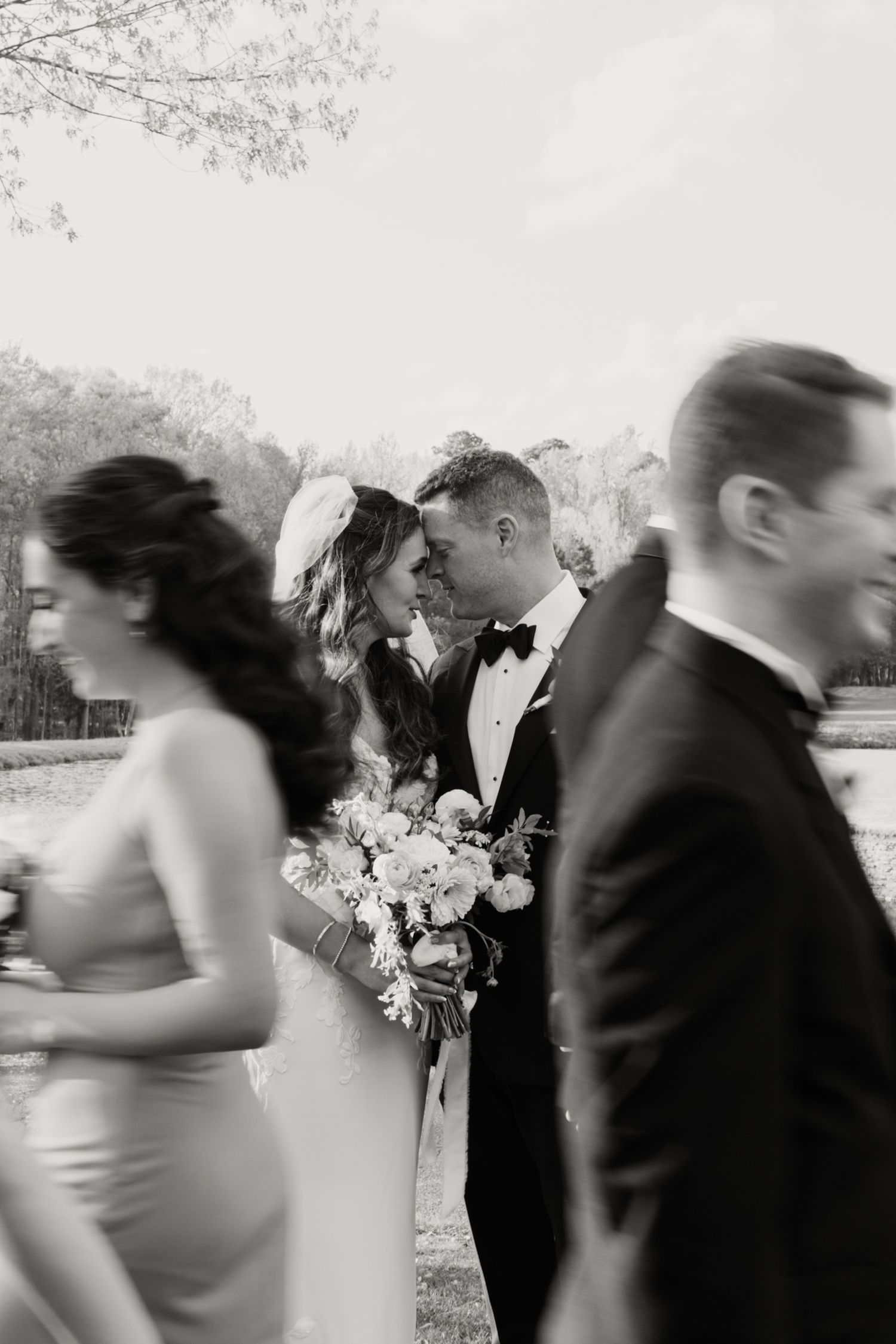 Motion-blurred wedding party walking outdoors with flowers and formal attire.