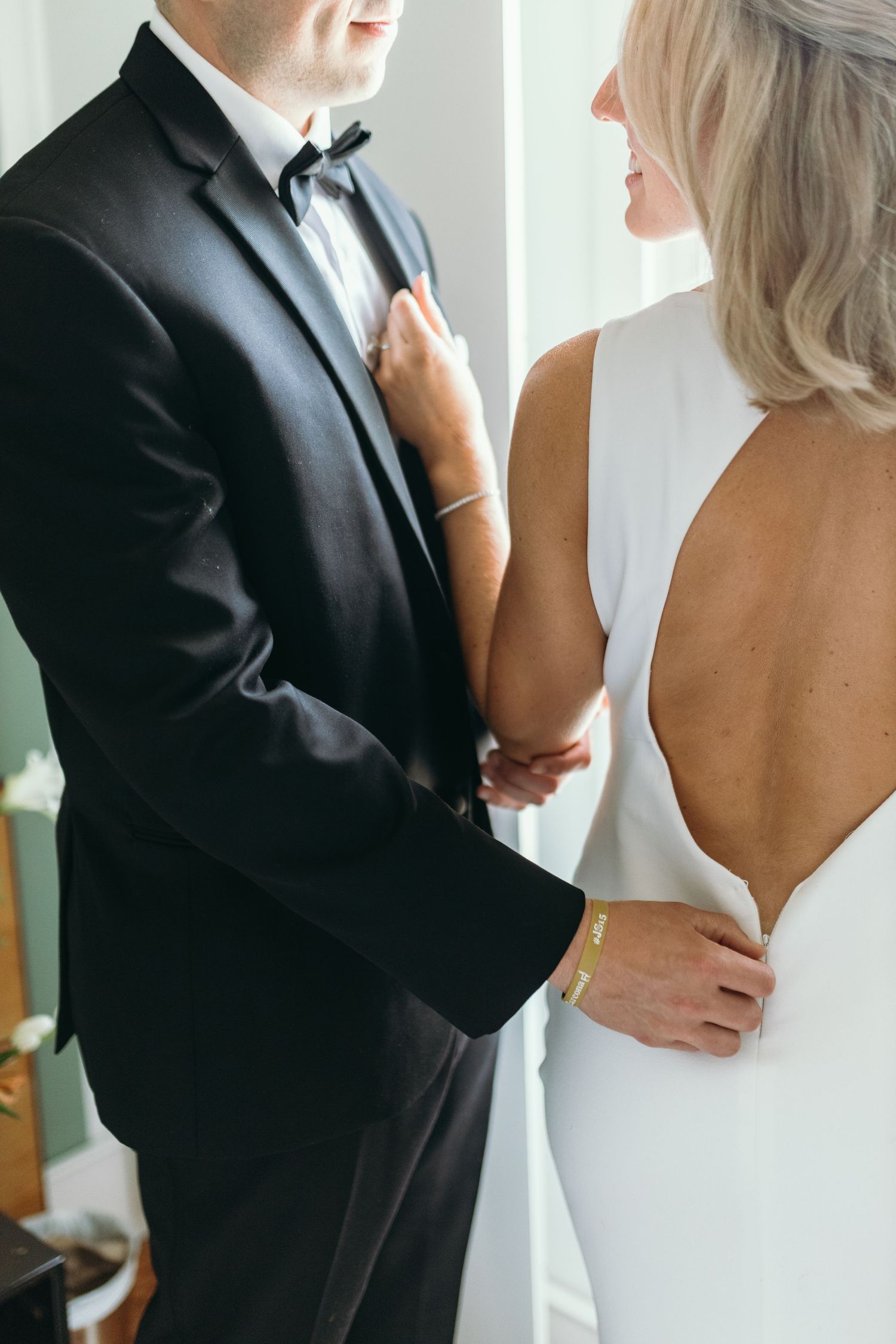 Close up of bride in backless white dress with groom in black tuxedo.