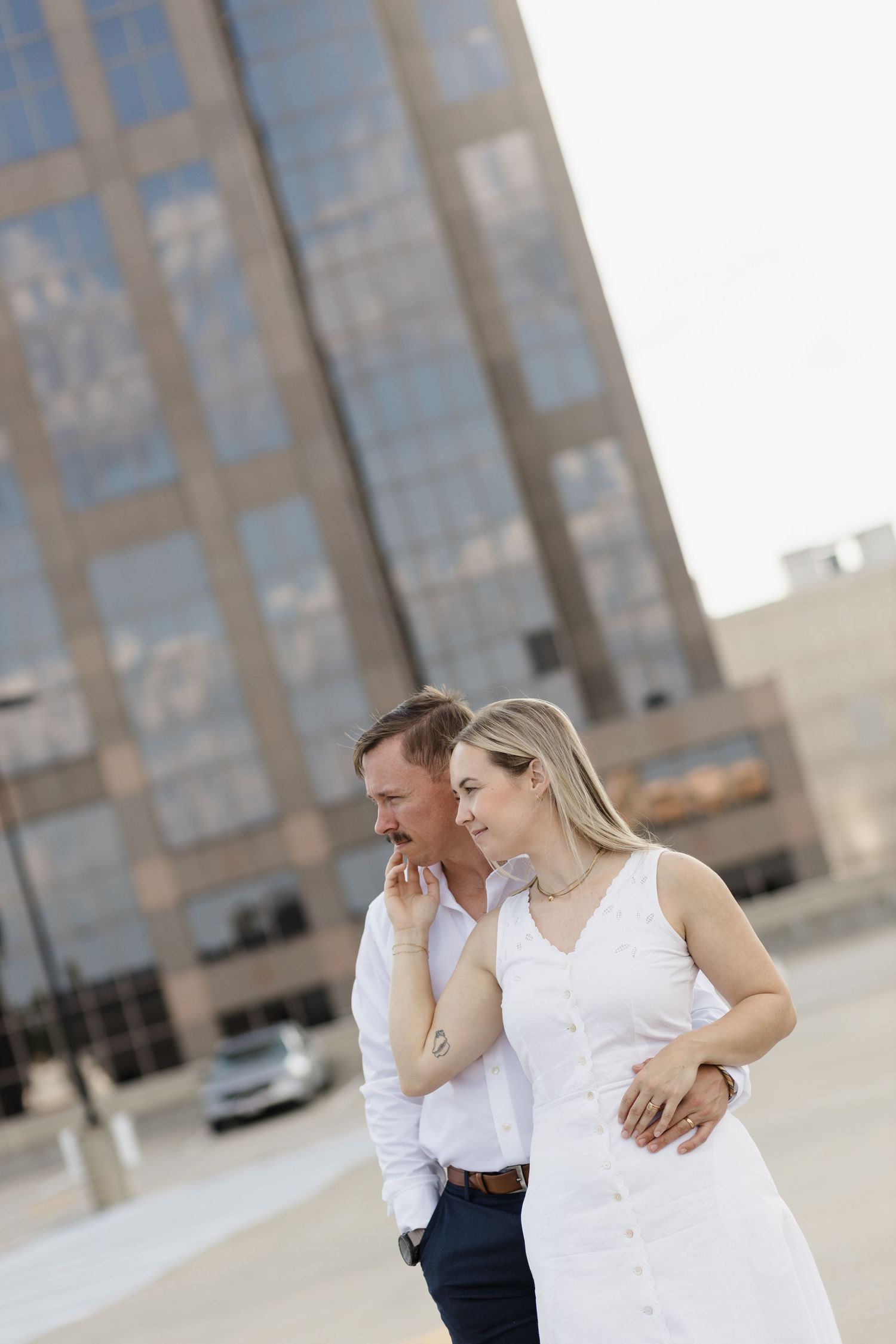 A couple walks together in an urban setting with modern glass buildings in the background.