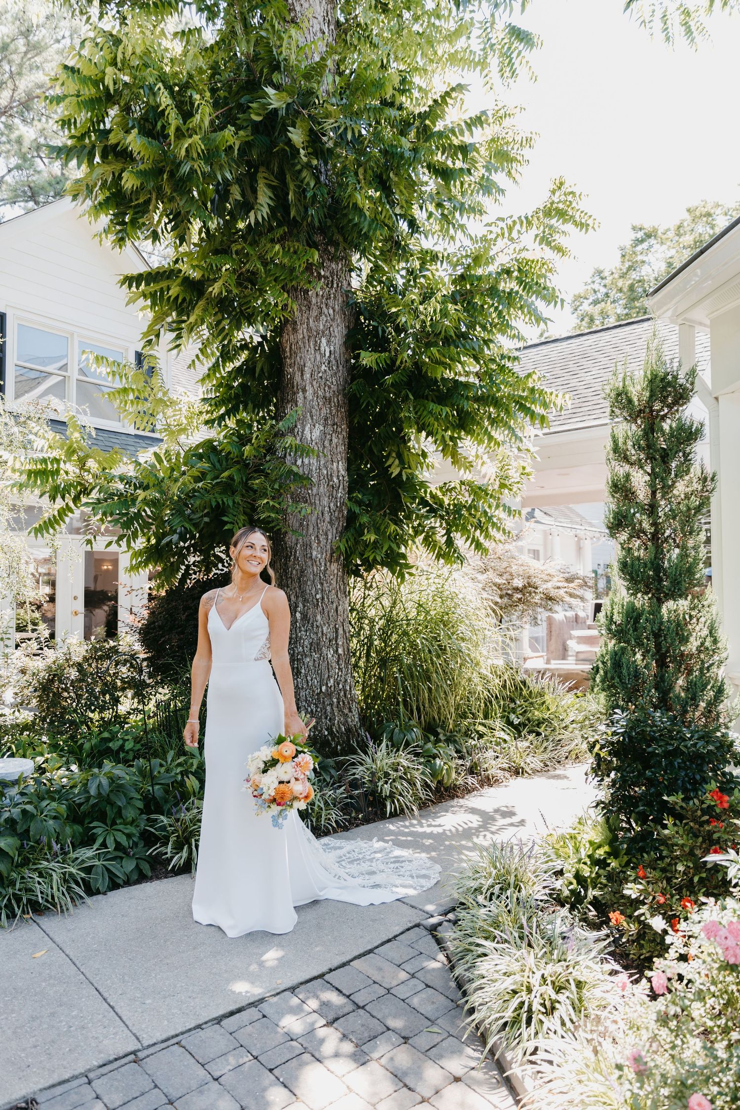 Elegant bride in white dress holding bouquet in lush garden setting.