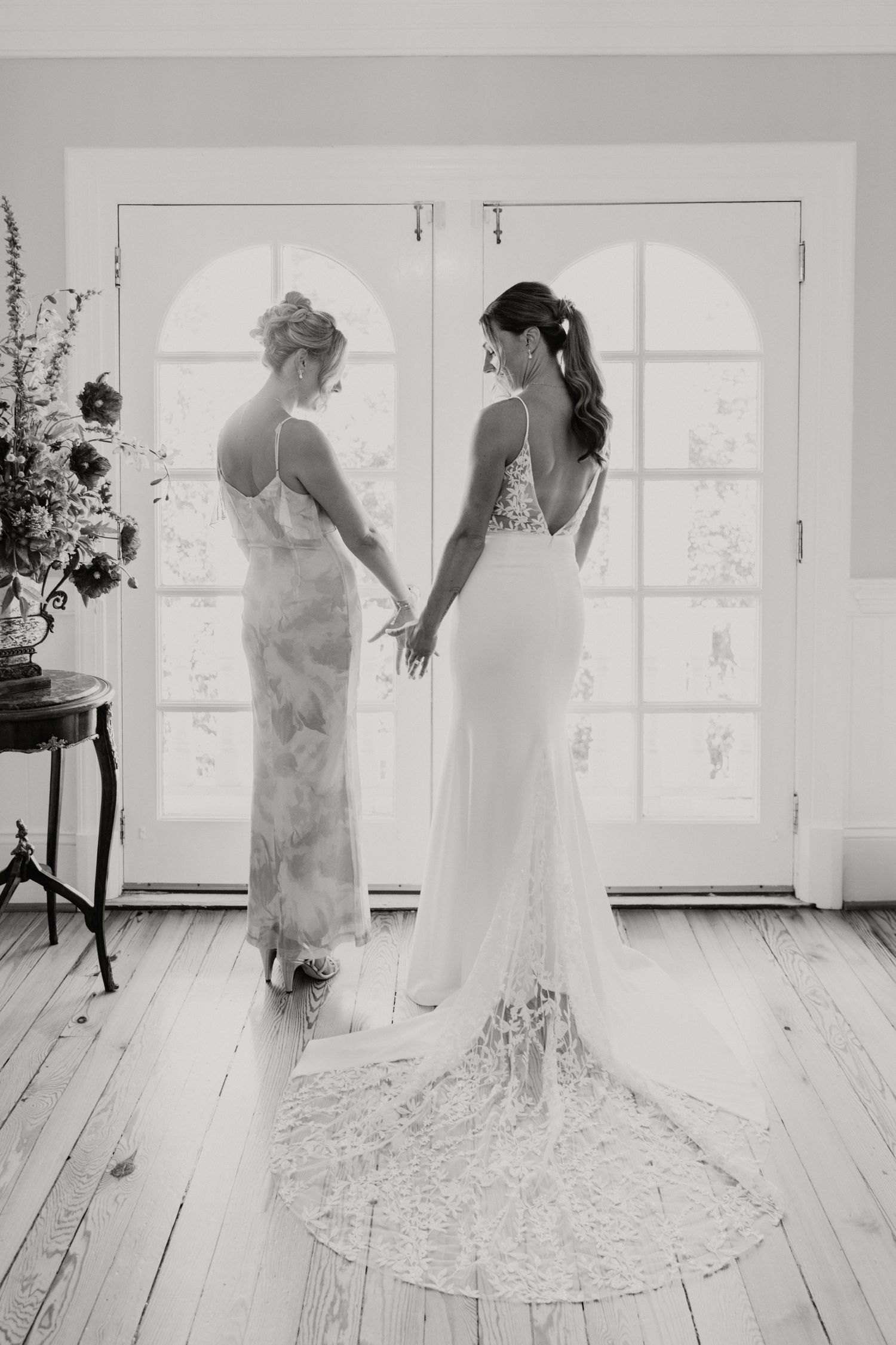 Two wedding dresses silhouetted against bright window in black and white.
