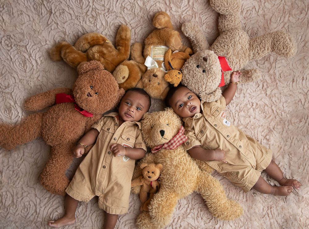 Twin babies in matching neutral jungle outfits surrounded by teddy bears during newborn photography session in central Florida.