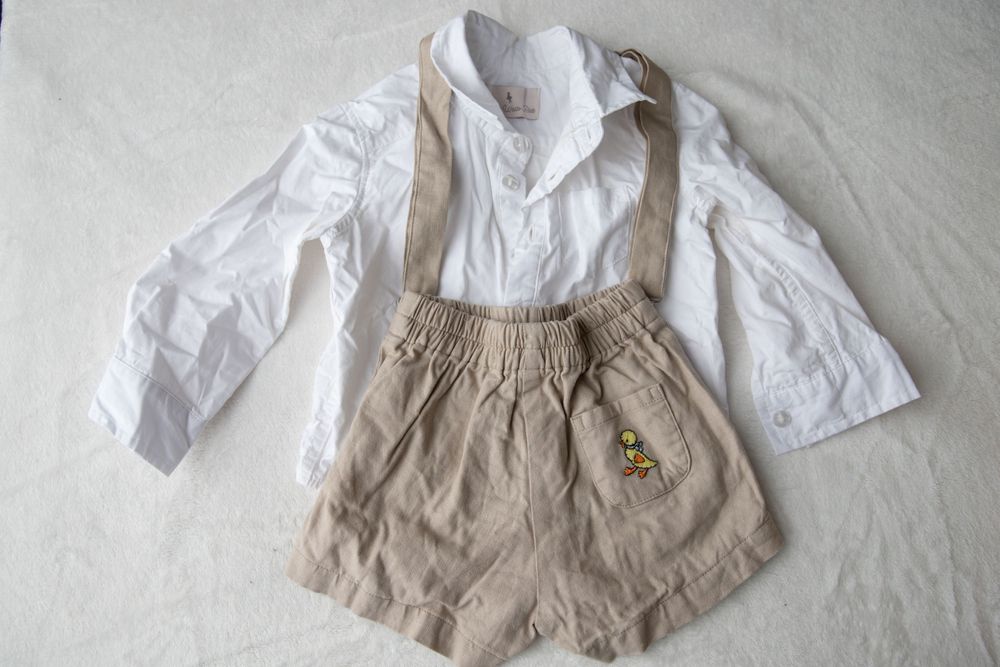 White long-sleeve button-up shirt with beige suspender shorts and embroidered patch for toddlers.