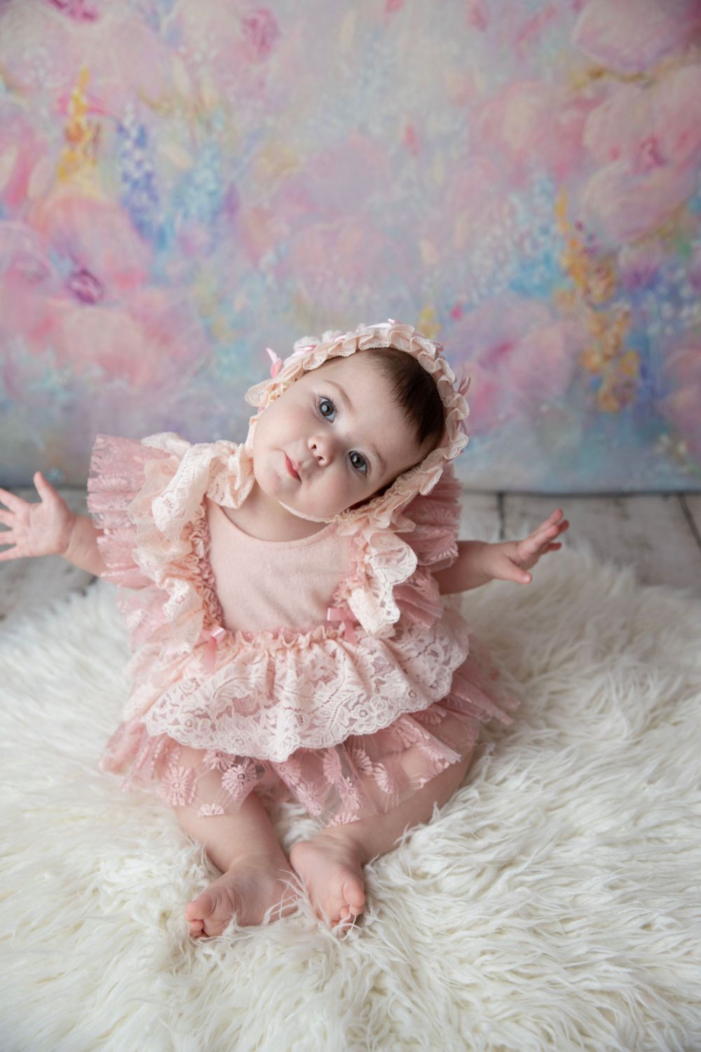 Baby girl in pink lace outfit sitting on soft fur during milestone photography session in Central Florida.