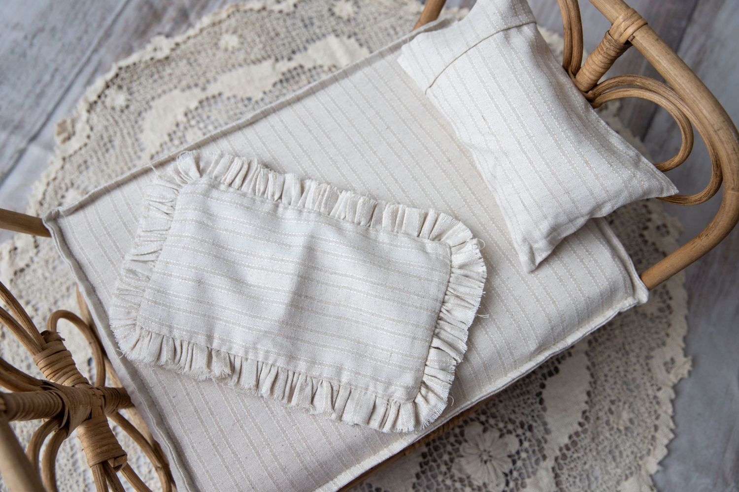 Cream striped ruffled newborn photography pillow set in a wicker basket on lace.