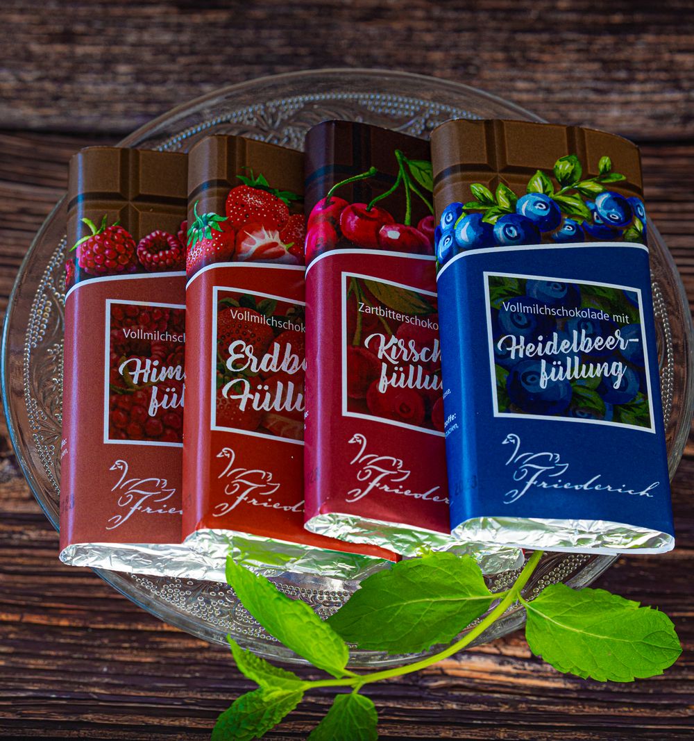 Foodfotogarfie. Collection of colorful chocolate bars with fruit flavors arranged on glass plate with green leaves.