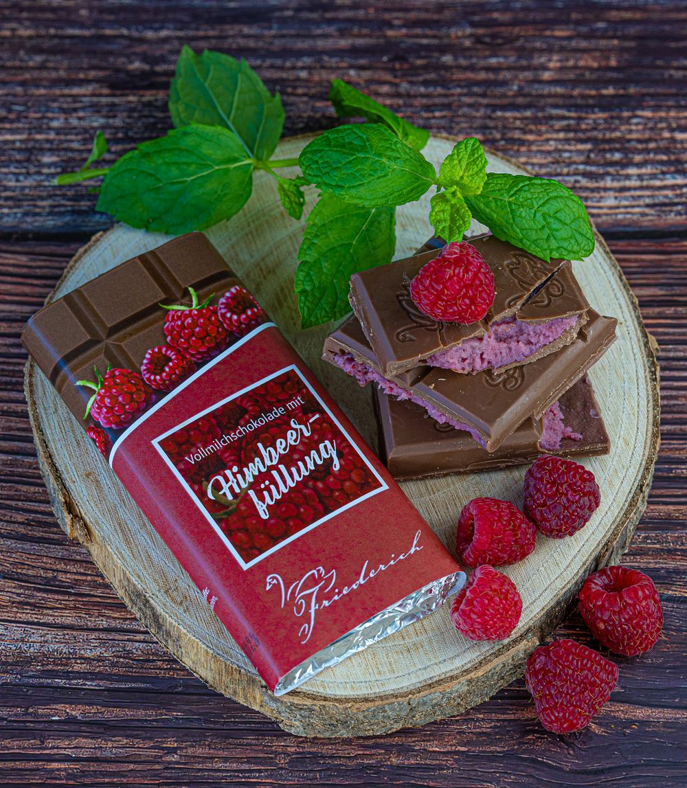 Food Fotografie - Red chocolate bar with fresh raspberries and chocolate pieces on wooden slice.