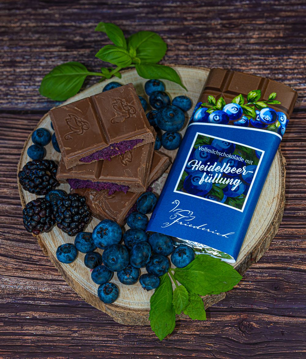 Foodfotografie. Chocolate bar with fresh blueberries and green leaves on wooden serving board.